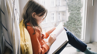 Barn sitter i fönster och läser.