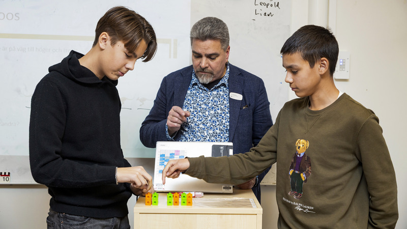 Två elever visar en uppgift de håller på med. De pekar på små blåa och gula pluppar på ett bord.