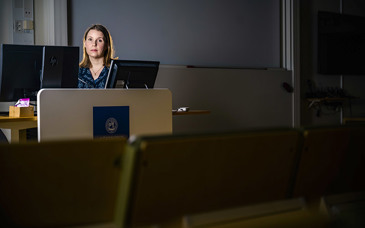 En kvinnas ansikte syns bakom dataskärmar i ett rum.