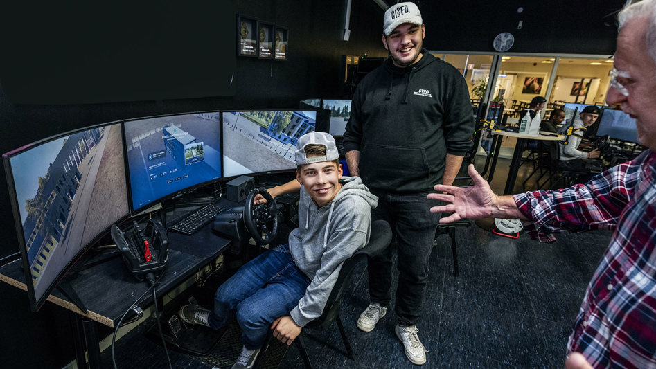 Två entusiastiska elever och lärare i ett klassrum med en körsimulator.