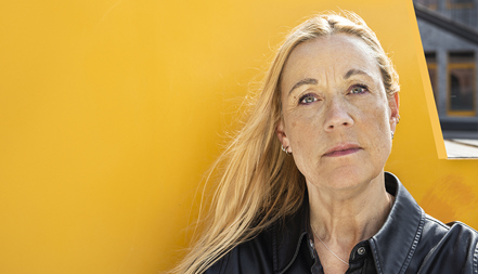 Kvinna med bestämd min som står framför gult föremål utomhus.