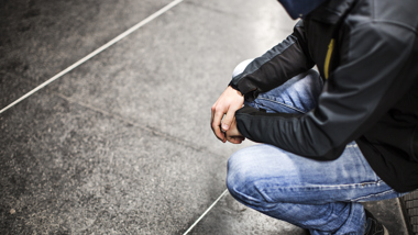 Ungdom som utstrålar utsatthet sitter på huk på ett grått stengolv