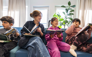 Lovisa Thelander sitter i en soffa med sina elever, alla har varsin bok.