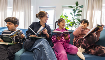 Lovisa Thelander sitter i en soffa med sina elever, alla har varsin bok.