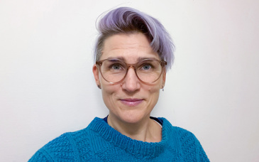 Närbild på en leende kvinna med blå tröja och glasögon.