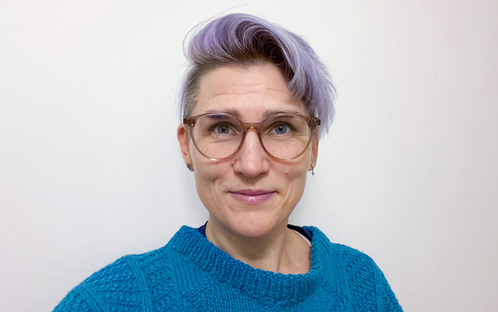 Närbild på en leende kvinna med blå tröja och glasögon.