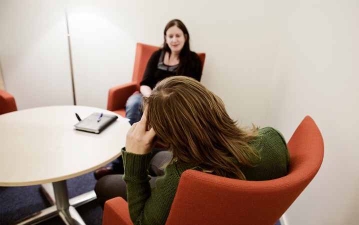 Två personer sitter i röd fåtöljer. Den ena sitter med ryggen mot kameran och hänger på armstödet.