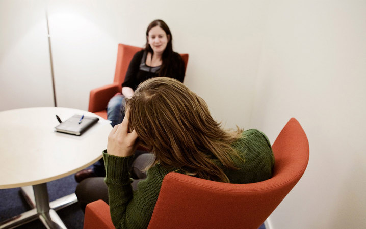 Två personer sitter i röd fåtöljer. Den ena sitter med ryggen mot kameran och hänger på armstödet.