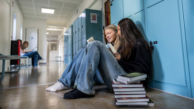 Två elever sitter i en skolkorridor och pratar.