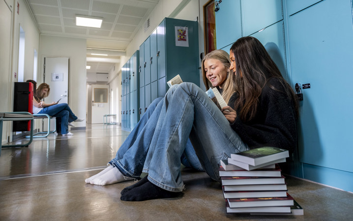 Två elever sitter i en skolkorridor och pratar.