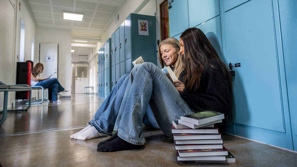 Två elever sitter i en skolkorridor och pratar.