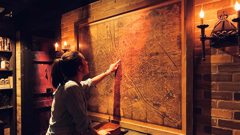 En kvinna pekar på en karta på en vägg i ett mörkt rum.