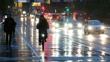 En cyklist, gångtrafikanter och bilar på en bro i regn och mörker.