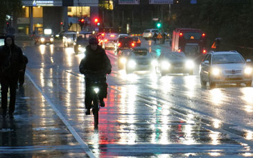En cyklist, gångtrafikanter och bilar på en bro i regn och mörker.