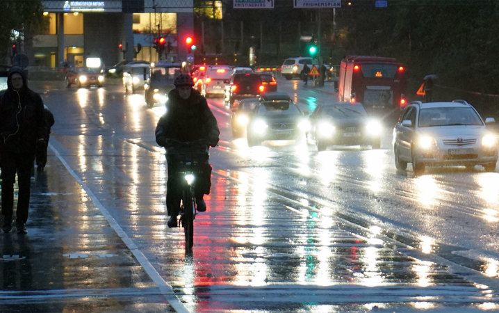En cyklist, gångtrafikanter och bilar på en bro i regn och mörker.