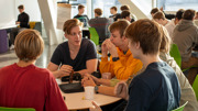 En grupp gymnasieungdomar sitter vid ett bord, diskuterar.