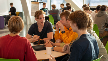 En grupp gymnasieungdomar sitter vid ett bord, diskuterar.