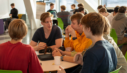 En grupp gymnasieungdomar sitter vid ett bord, diskuterar.