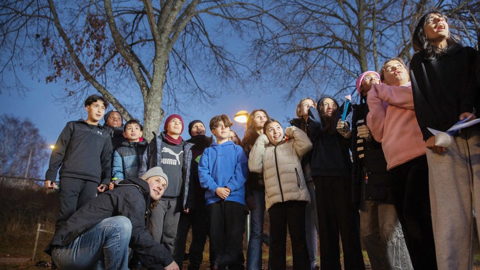 Elever utomhus som tittar upp mot himlen tillsammans med sin lärare. 