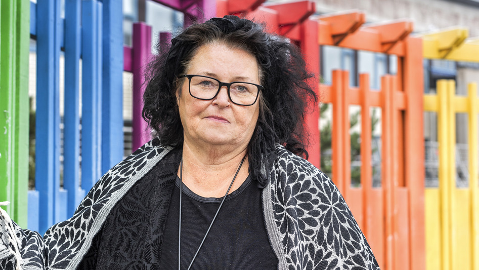 Närbild på en kvinna som står utomhus framför ett staket som är målat i regnbågens färger.