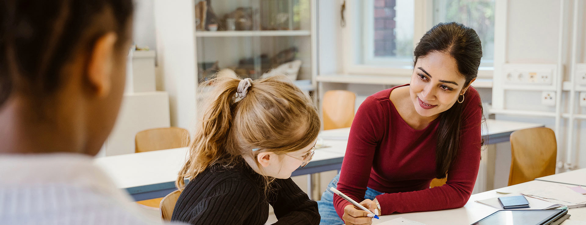 Lärare visar något för barn, båda sitter vid bänk.