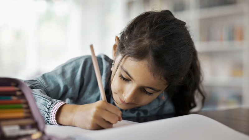 En flicka skriver med en penna på ett papper.