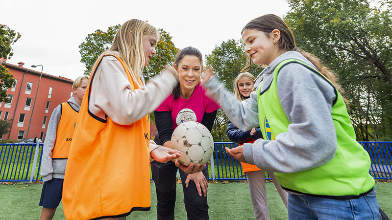 Barn i färgglada västar som spelar fotboll.