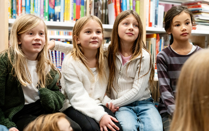 Barn sitter i ett bibliotek och lyssnar på någon som pratar.