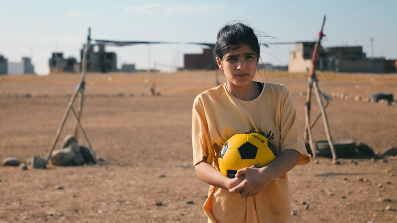 En flicka med en gul fotboll i famnen.