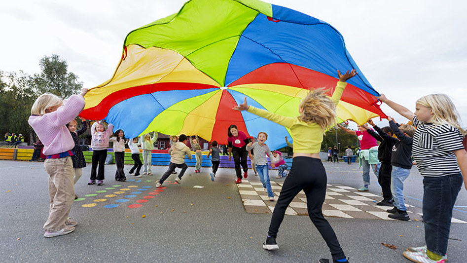 Barn på skolgård som leker med färgglatt skynke. 