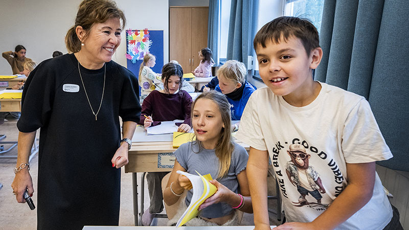 Glada elever och lärare i ett färgglatt klassrum.