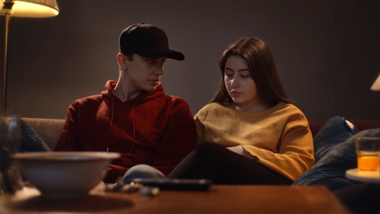 Två ungdomar sitter bredvid varandra i en soffa.