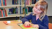 En flicka i ett biblioteket har handen på en bild i en bok. 