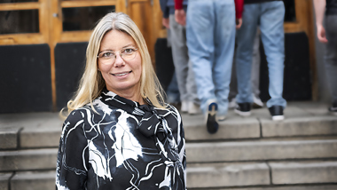 En rektor som står i trappan till skolans entré. Bakom rektorn är det elever som går in i skolan.