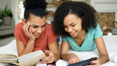 Två flickor ligger på mage och den ena pekar och visar på en skärm.